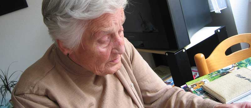 Eine alte Frau sitzt in einem Zimmer an einem Tisch und liest. (c) Pixabay.om