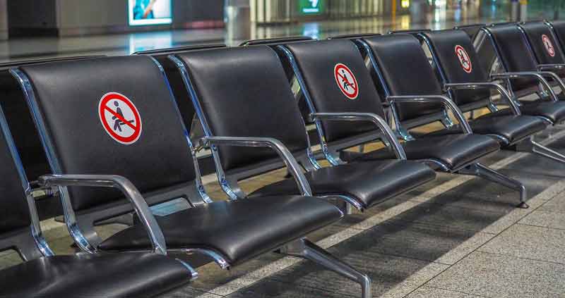Eine Sitzreihe auf einem Flughafen, bei der auf jedem 2. Sitz ein "Nicht hinsetzen" Pickerl klebt.
(c) Pixabay.com