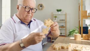 Ein älterer Mann mit großen Holzpuzzlesteinen. (c) AdobeStock