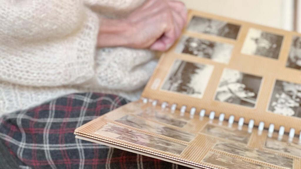 Die Hand einer alten Frau, die in einem Fotoalbum blättert. (c) AdobeStock