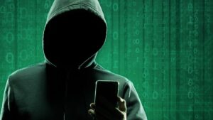 Ein anonymer Hacker mit Kapuzenpulli über dem Kopf schaut auf sein Smartphone. (c) AdobeStock