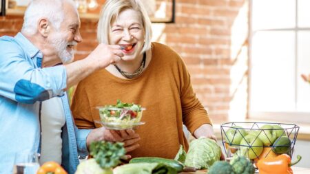 Ein älteres Paar in der Küche; der Mann "füttert" die Frau mit einem Paradeiser. (c) AdobeStock